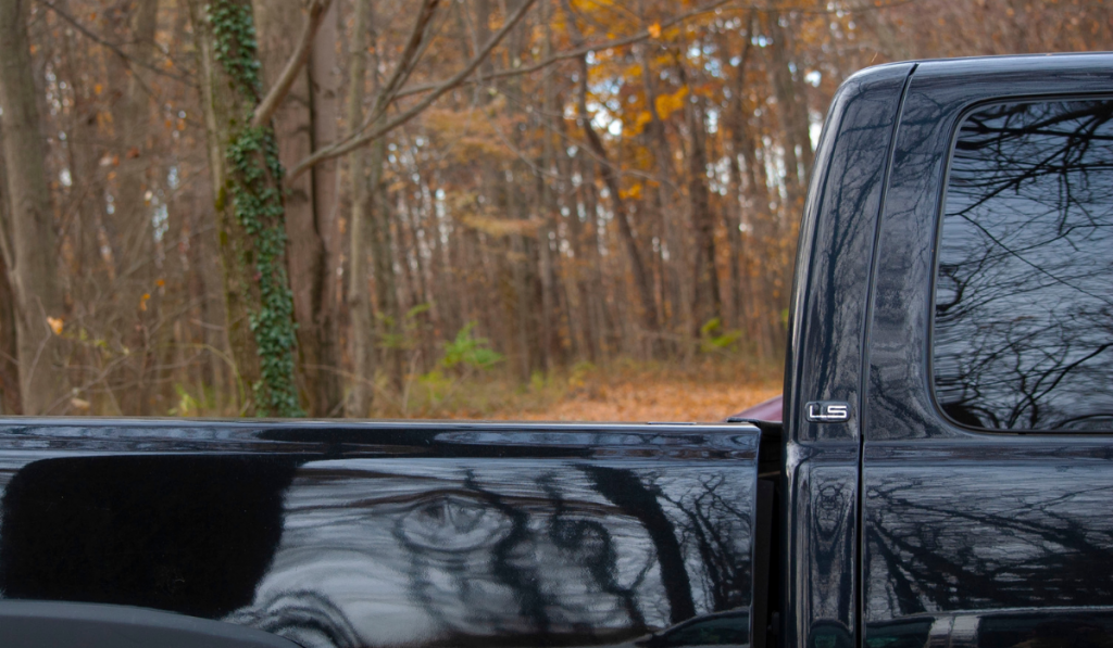 A black LS pickup truck with background of autumn trees with one tree bark covered in ivy.
