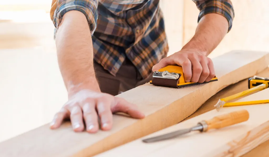 Concentrated young male carpenter sanding wood in his workshop