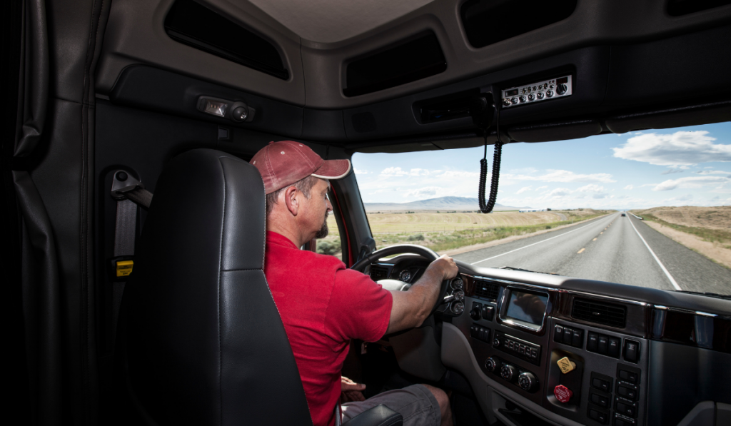 Interior cab view of a Caucasian man driving his commercial truck.