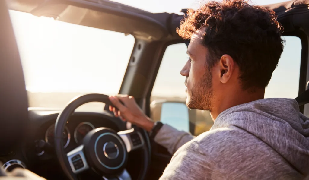 Side view of young Hispanic man driving with sunroof open