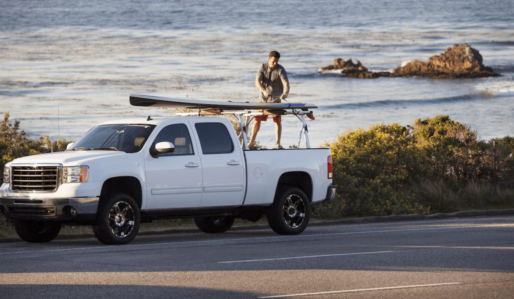 man removing his surfboard on pickup truck parked at riverside 